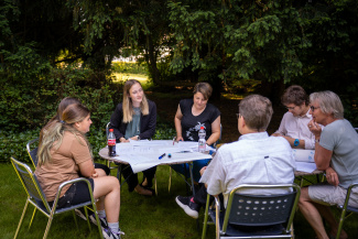 Eine Gruppe sitzt im Garten und diskutiert über das Anliegen von einem Jugendtreff. 