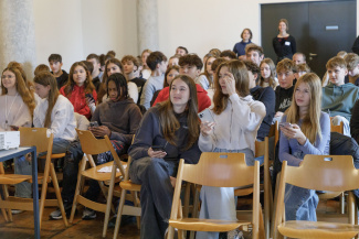 Jugendliche sitzen auf Stühlen und beantworten einen Quiz auf ihren Handys.