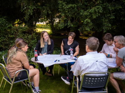 Eine Gruppe sitzt im Garten und diskutiert über das Anliegen von einem Jugendtreff. 