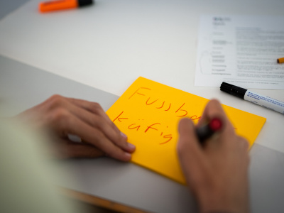 Jemand schreibt auf ein gelbes Post-It: Fussball-Käfig