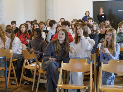 Jugendliche sitzen auf Stühlen und beantworten einen Quiz auf ihren Handys.